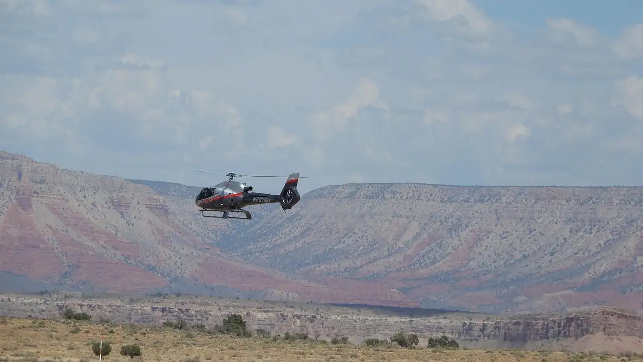 Small helicopter flying past a layered plateau above desert scrub