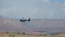 Small helicopter flying past a layered plateau above desert scrub