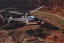 White helicopter flying over red canyon country with a river bend below