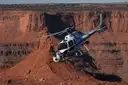 White helicopter banking over red cliffs and buttes