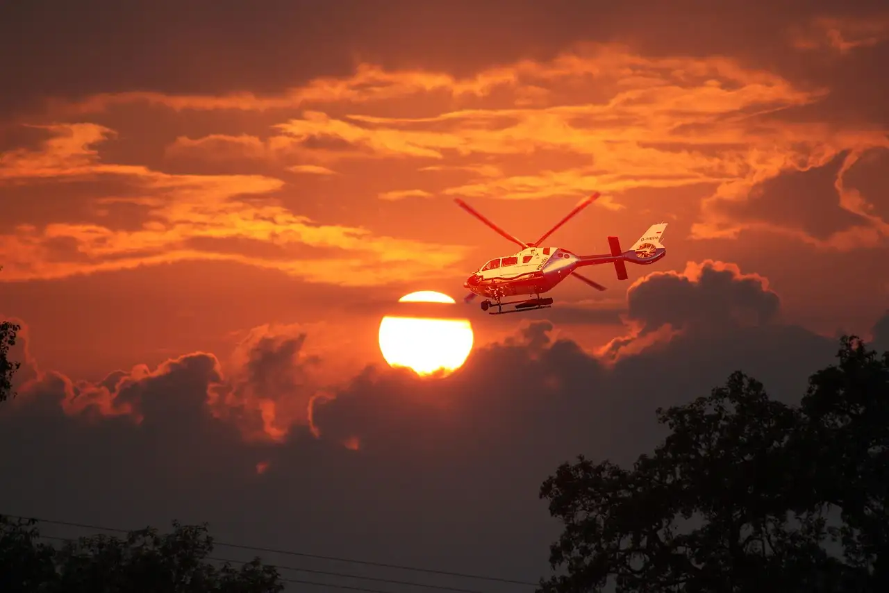 Red and white helicopter flying past the setting sun
