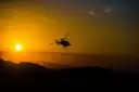 Helicopter in silhouette over dark hills at sunset