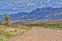Dirt road through Joshua trees and desert scrub toward long layered cliffs