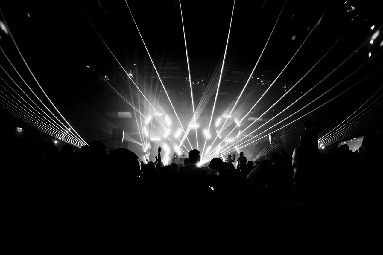 Laser beams fanning over a stage above a crowd in silhouette, black and white
