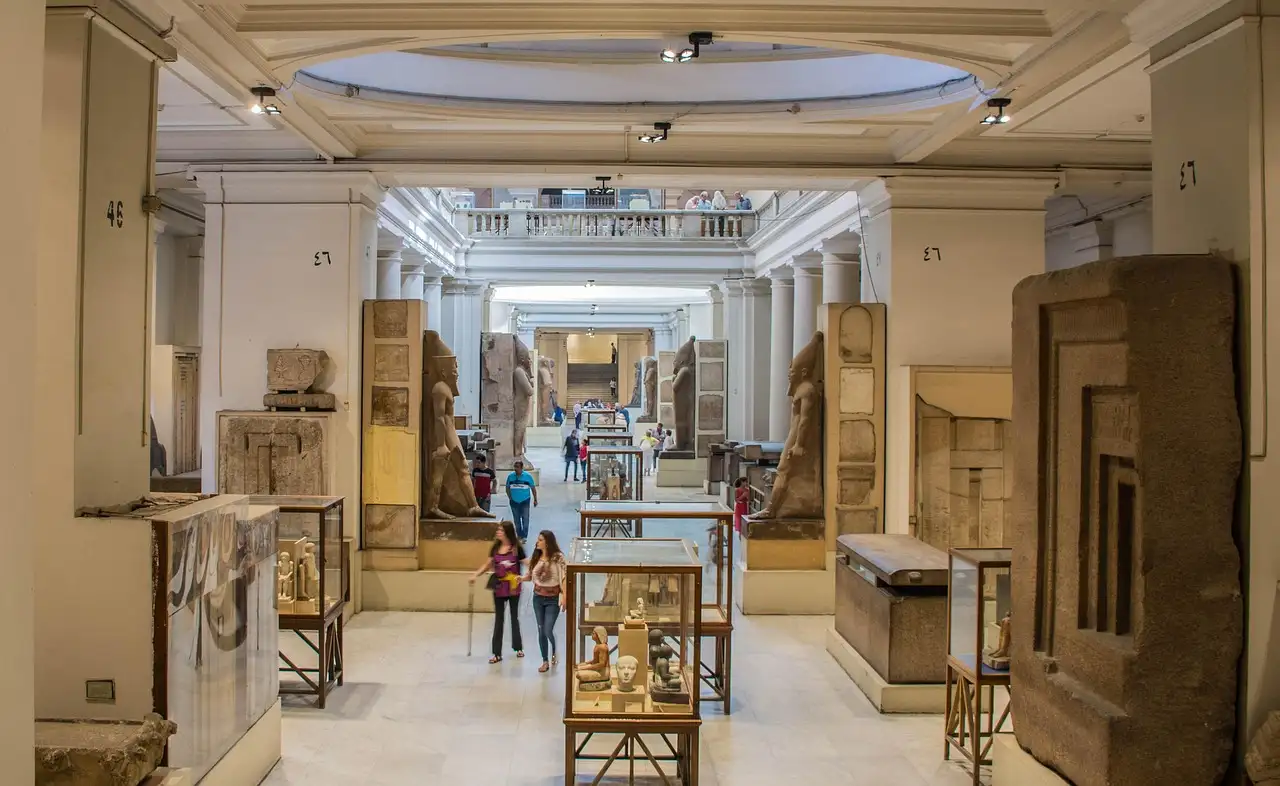 Long museum hall with glass display cases and stone statues, a few visitors in the distance