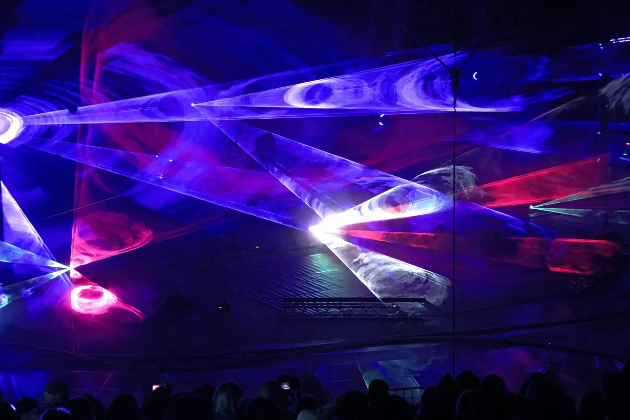 Blue and pink laser beams sweep over a dark hall above a silhouetted crowd