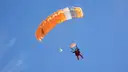 Skydiver under an orange and white parachute in a blue sky