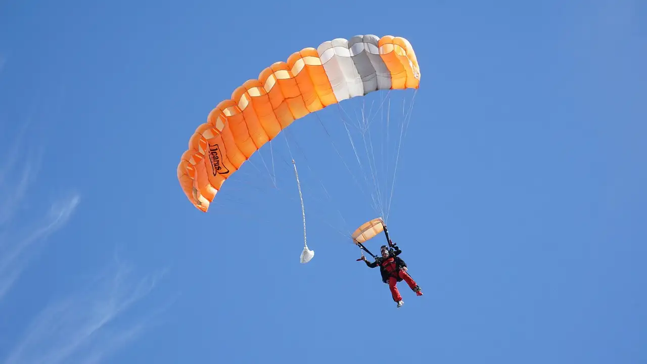 Skydiver under an orange and white parachute in a blue sky