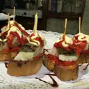Small bites on toast topped with peppers and sauce, held by skewers