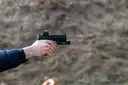 Two hands aiming a pistol at an outdoor range