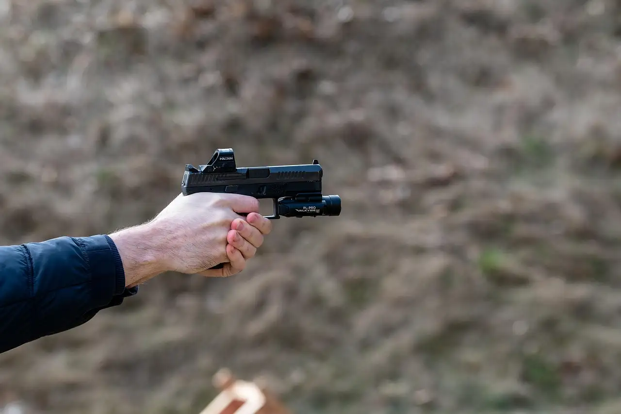 Two hands aiming a pistol at an outdoor range