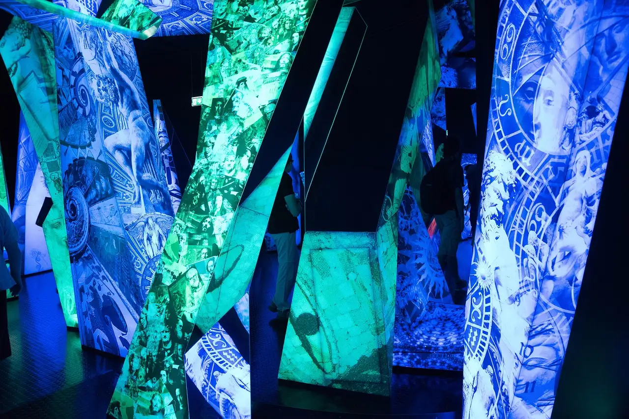 Dark exhibition room with tall panels glowing in blue and green projected artwork