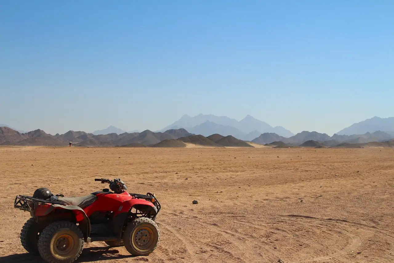 Red ATV parked on open desert with jagged mountains beyond