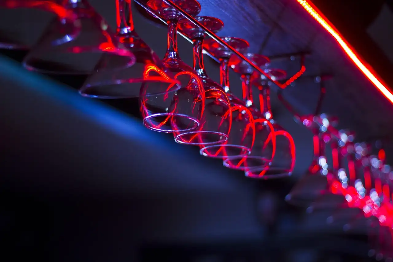 Glasses hanging from a bar rack in red and blue light