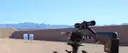 Scoped rifle on a shooting rest at a desert range with targets and mountains