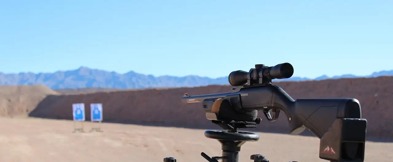 Scoped rifle on a shooting rest at a desert range with targets and mountains
