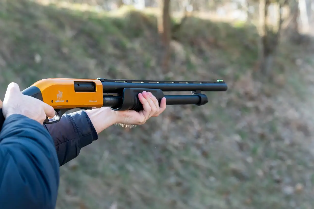Hands holding a pump-action shotgun at an outdoor range