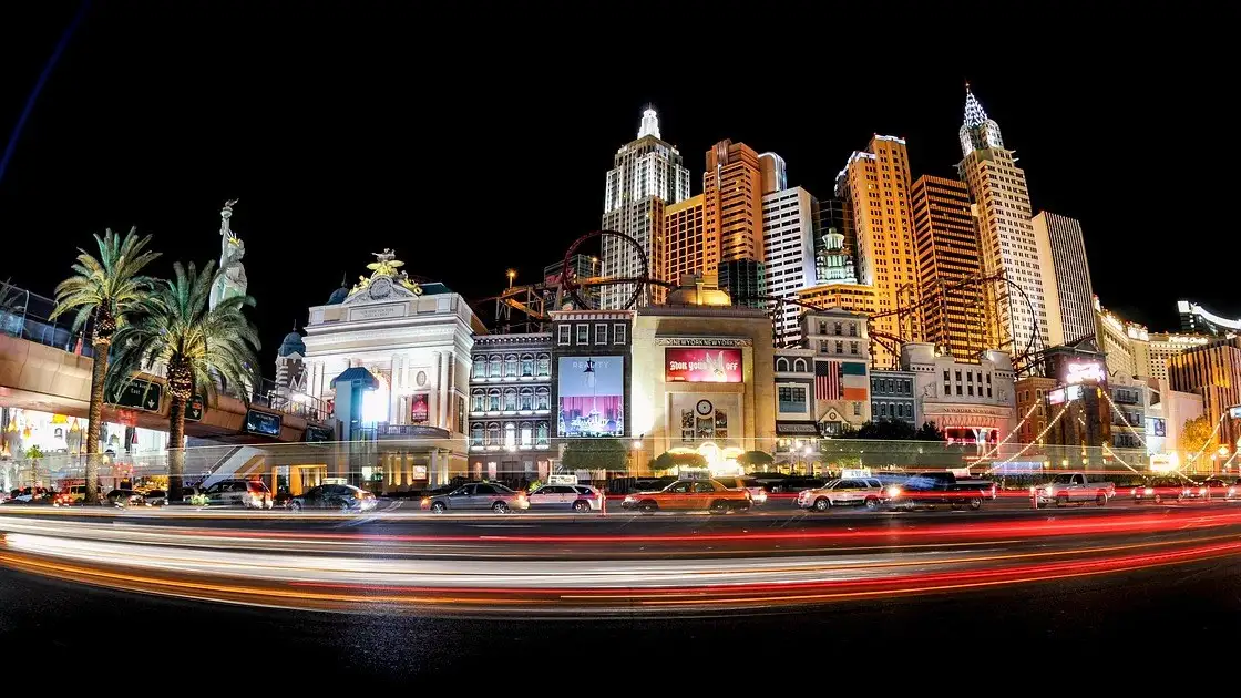 Car light trails streak along the Las Vegas Strip at night past a lit New York-style resort facade