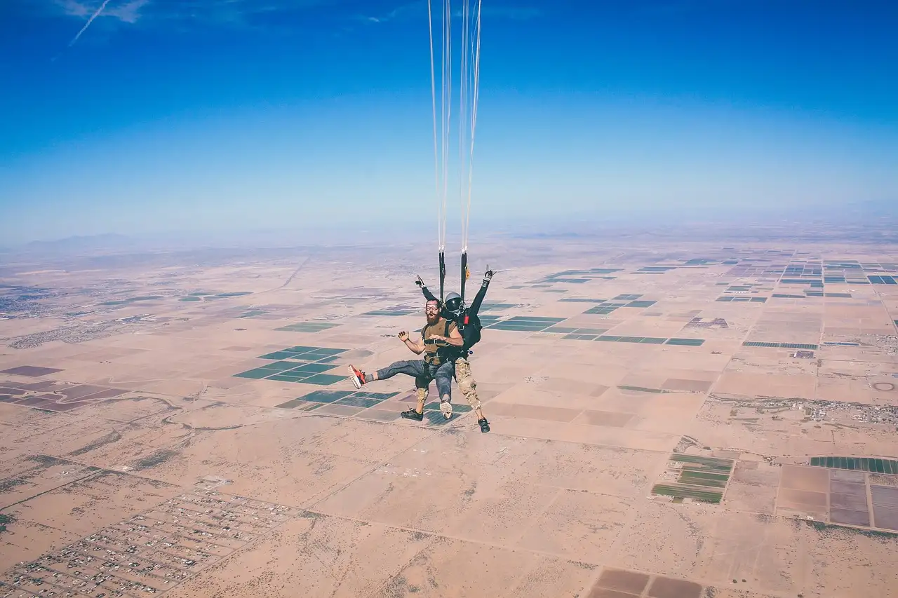 Tandem skydivers under a parachute high above flat desert land