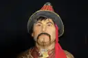 Wax figure of a Mongol warrior in a red hat and embroidered robe against a dark backdrop