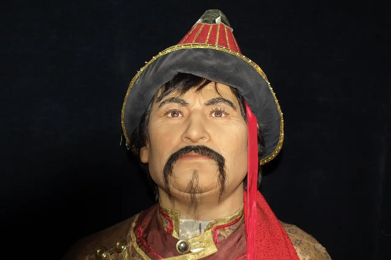 Wax figure of a Mongol warrior in a red hat and embroidered robe against a dark backdrop