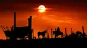 Silhouettes of a covered wagon, a horse and a rider against a red sunset