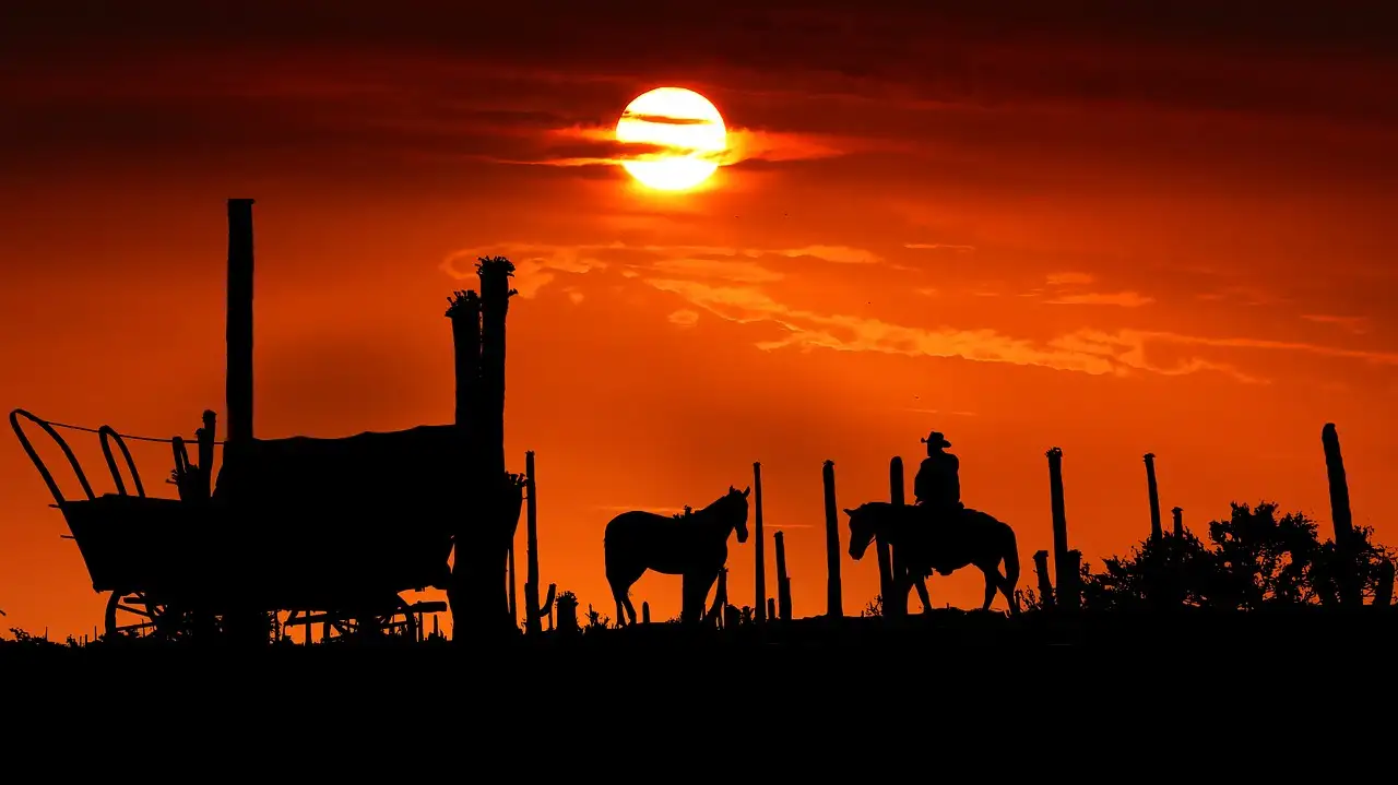 Silhouettes of a covered wagon, a horse and a rider against a red sunset