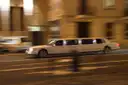 White stretch limousine driving down a lit city street at night, background blurred by motion