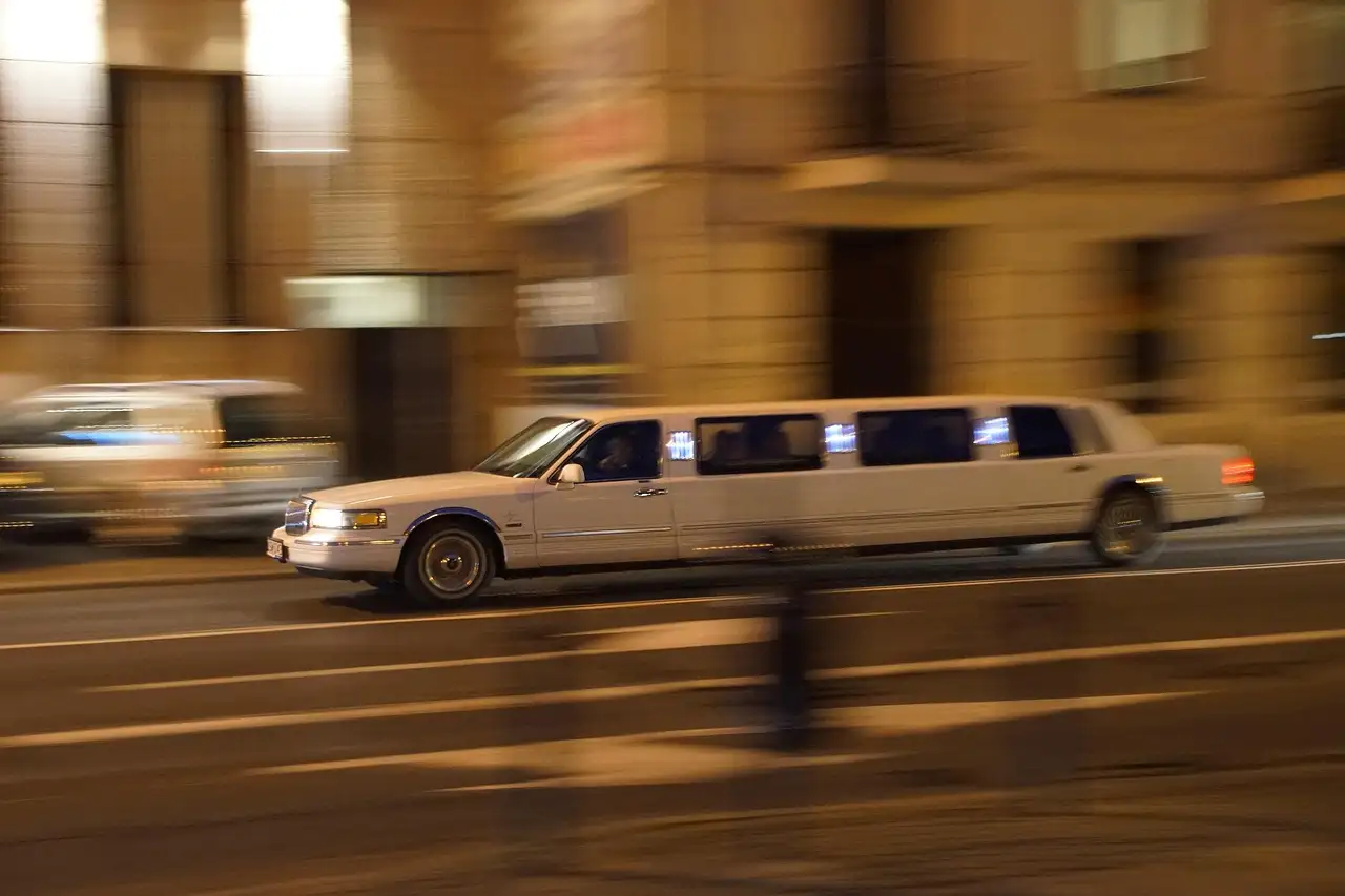White stretch limousine driving down a lit city street at night, background blurred by motion