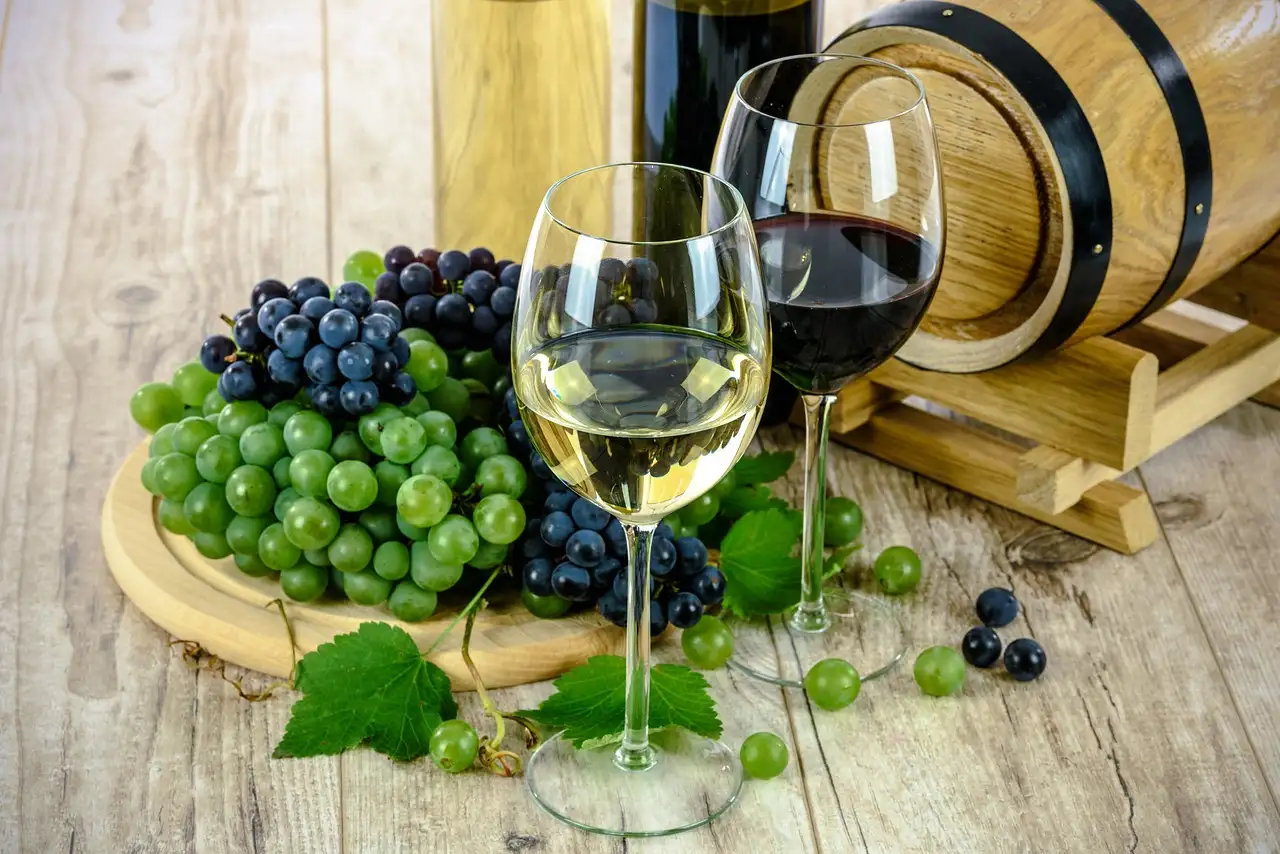 White and red wine glasses beside grapes and a small barrel