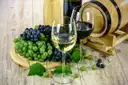 White and red wine glasses beside grapes and a small barrel