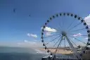 Two riders on a zip line beside a big wheel over a beach