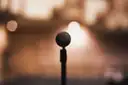 A stand microphone on a stage in front of a warm, blurred stage light
