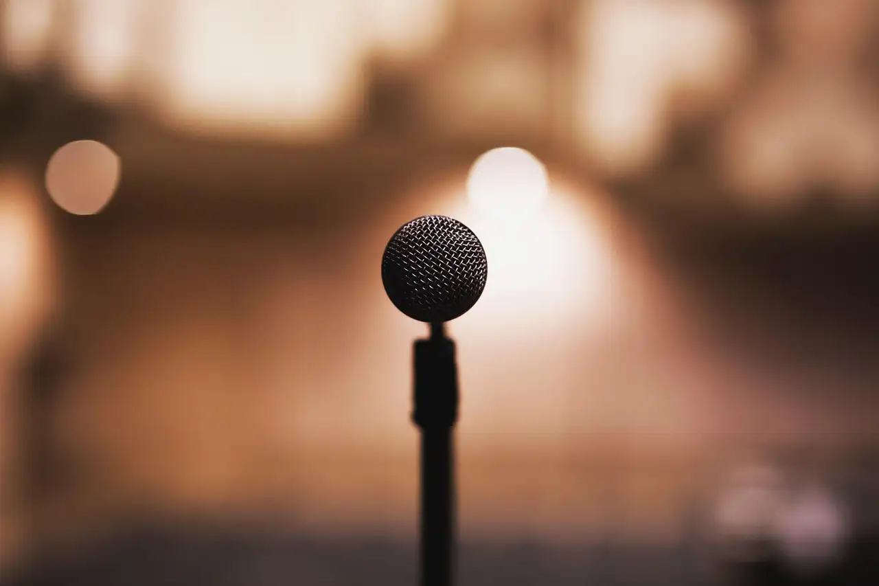 A stand microphone on a stage in front of a warm, blurred stage light