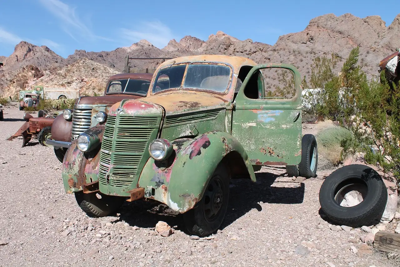 A rusted old pickup truck parked among desert rocks and scrub