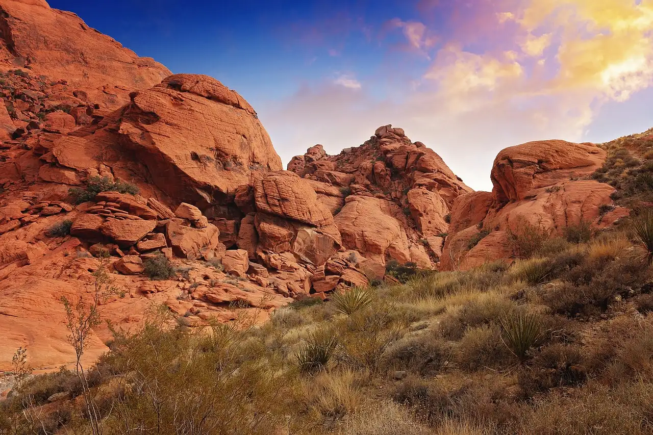 Red sandstone boulders and desert grass under a colorful sunset sky