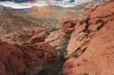 Red sandstone rocks and desert scrub in a wide valley, with paler mountains behind
