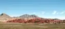 A low red sandstone ridge across a green desert plain, with gray mountains behind