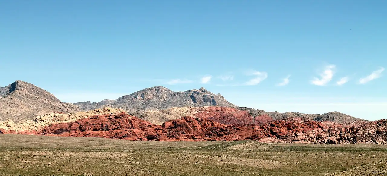 A low red sandstone ridge across a green desert plain, with gray mountains behind