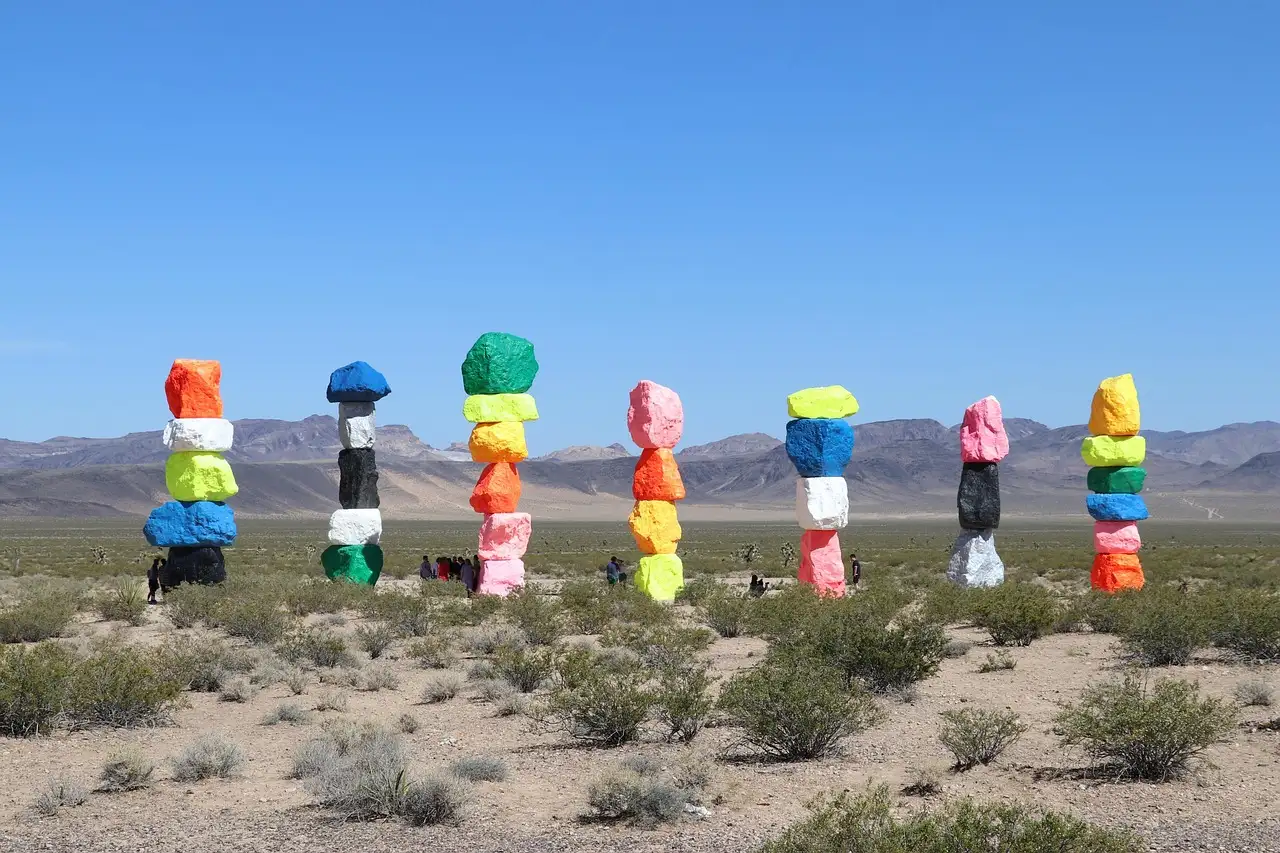 Seven tall stacks of brightly painted boulders standing in the Mojave Desert below dry mountains