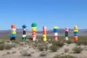 Seven tall stacks of brightly painted boulders standing in the Mojave Desert below dry mountains
