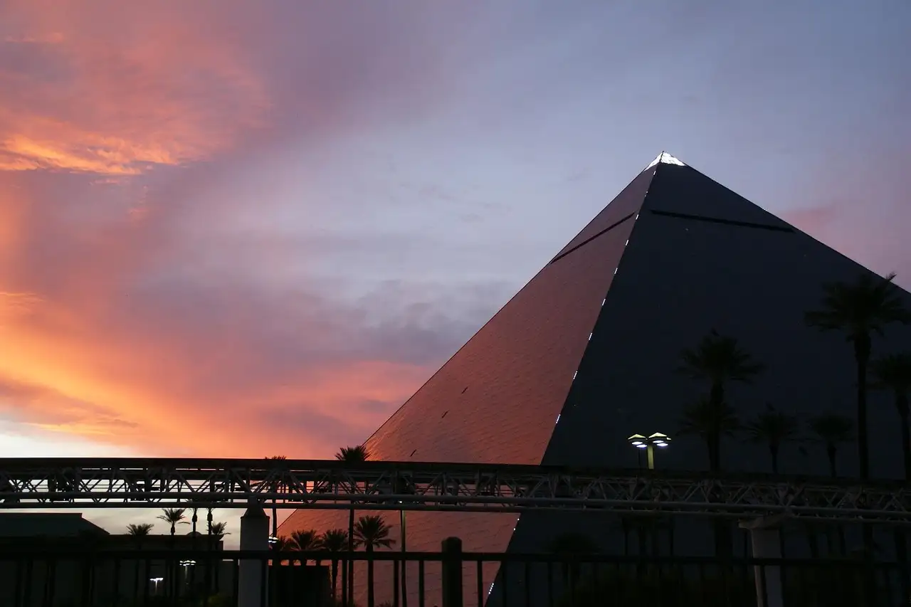 The Luxor's dark glass pyramid against a pink sunset sky, palm trees and a monorail track in front