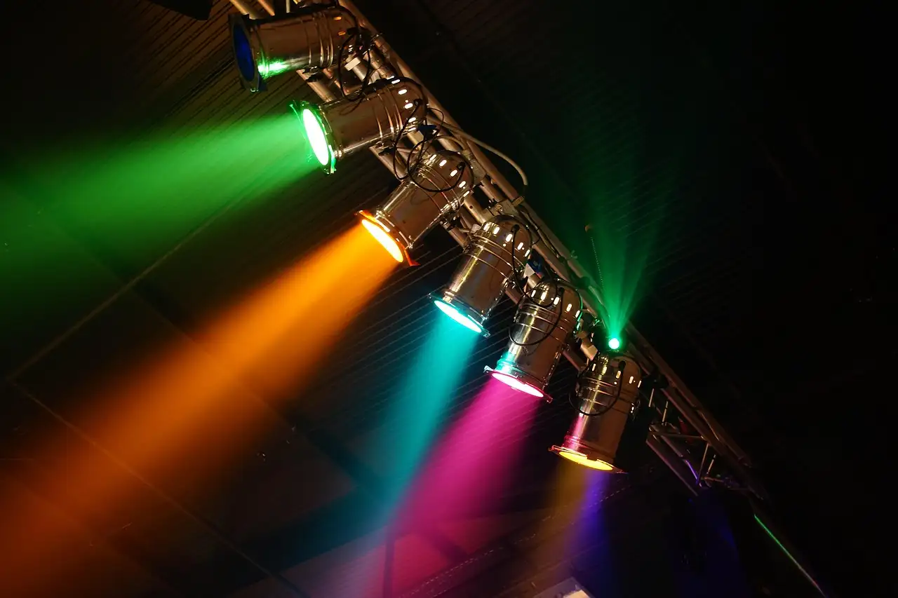 Stage spotlights on a truss shining green, orange, pink and purple beams through haze