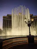 The Bellagio fountains lit at dusk in Las Vegas, with a lamp post in the foreground