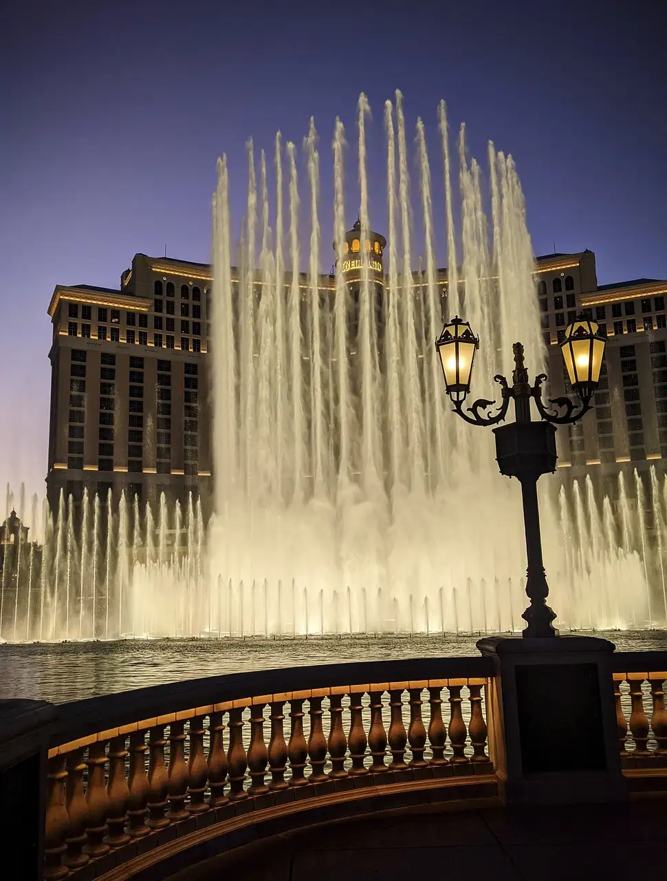 The Bellagio fountains lit at dusk in Las Vegas, with a lamp post in the foreground