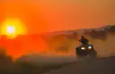 A rider on a quad bike kicking up dust at sunset on a dirt road