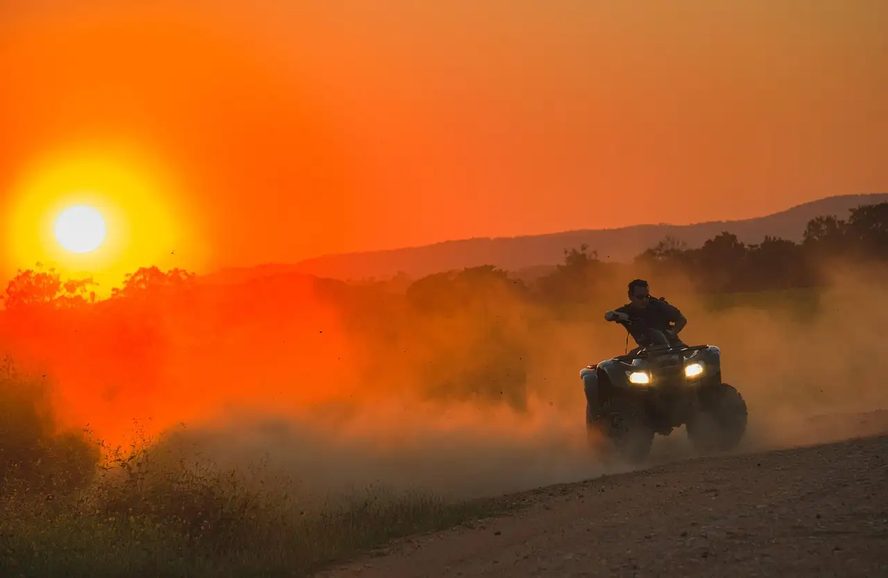 A rider on a quad bike kicking up dust at sunset on a dirt road