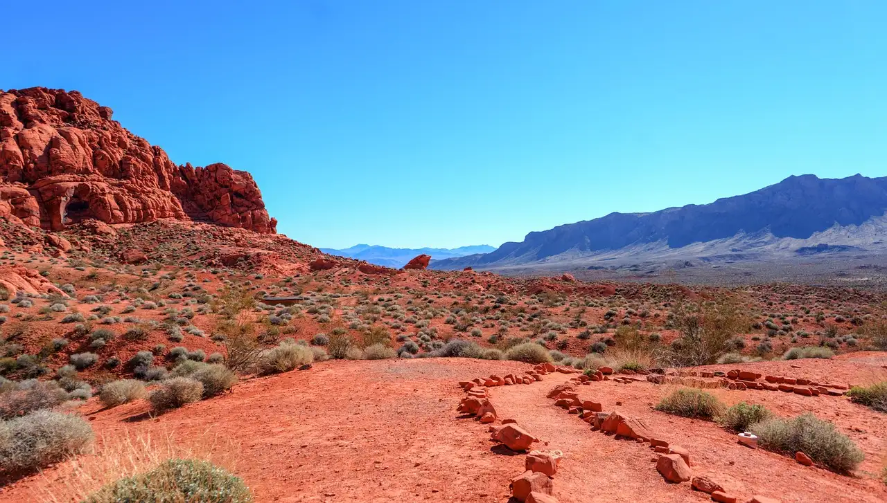 Red sandstone and red desert ground with blue mountains on the horizon