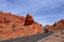 A red car on the curving road between red sandstone rocks in Valley of Fire