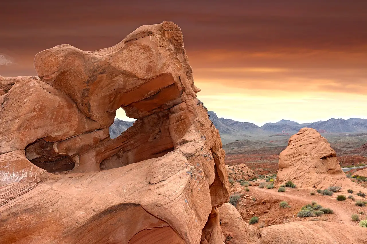 A red sandstone arch in Valley of Fire State Park under an orange evening sky